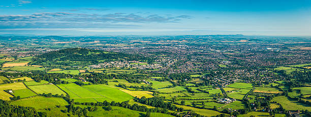 Aerial panorama over country town green fields and suburban housing Aerial panoramic vista over the green patchwork landscape of the Cotswold escarpment, pasture and farms, to the City of Gloucester, the Severn Vale and Welsh mountains beyond. ProPhoto RGB profile for maximum color fidelity and gamut. patchwork landscape photos stock pictures, royalty-free photos & images