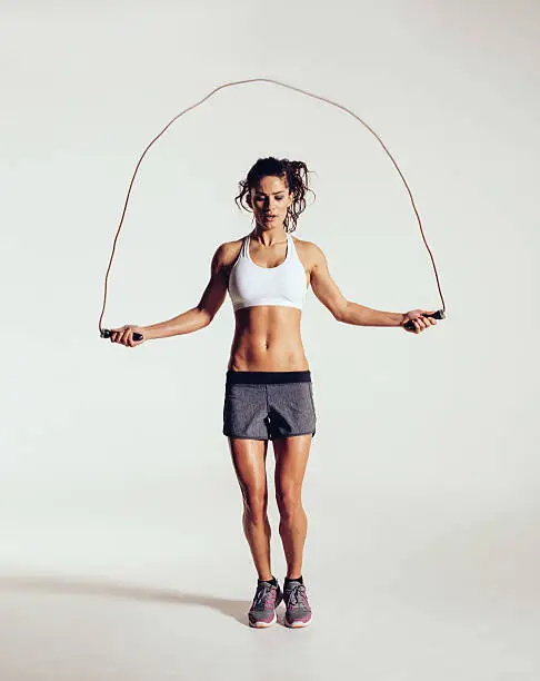 Fit young woman skipping rope. Portrait of muscular young woman exercising with jumping rope on grey white background.