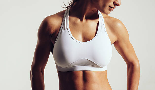 Fit woman in sports bra Portrait of fit woman in sports bra with muscular body against grey background. Close-up studio shot of female fitness model in sports wear. sports bra stock pictures, royalty-free photos & images