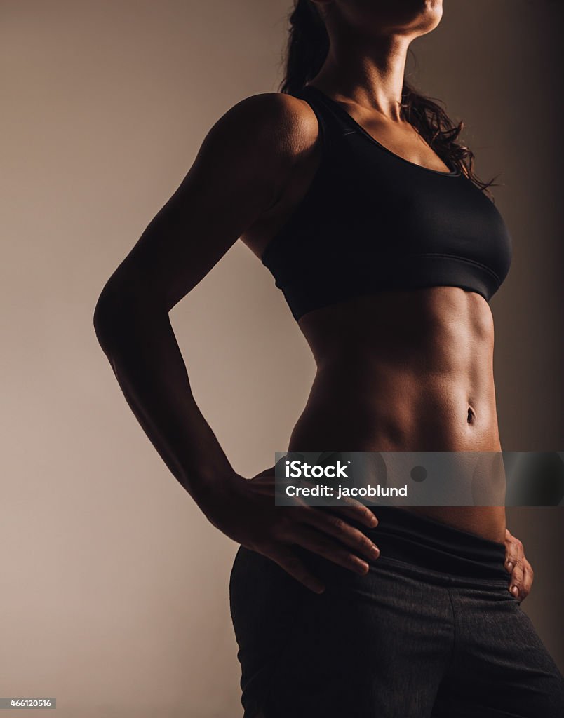 Muscular young woman posing in sportswear Cropped image of muscular young woman posing in sportswear. Fit female model with perfect torso in studio. 2015 Stock Photo