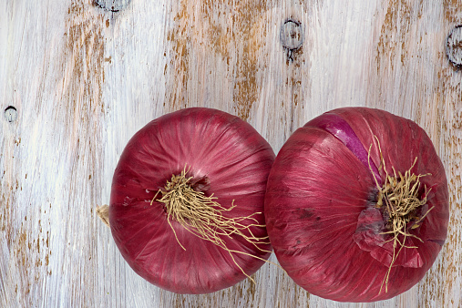Two red onions on the white painted wooden background.