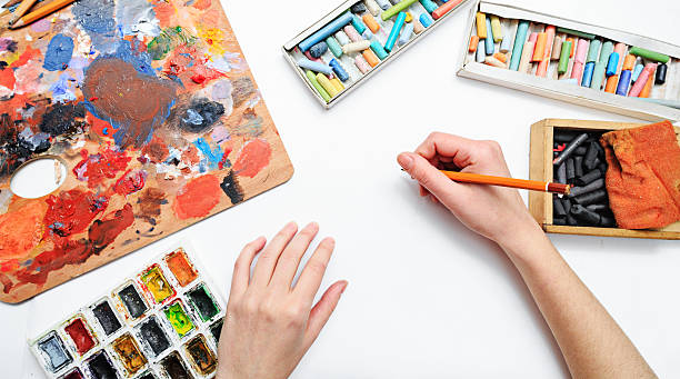istock Artist's hand at work, paints, brushes and pencils 466135254