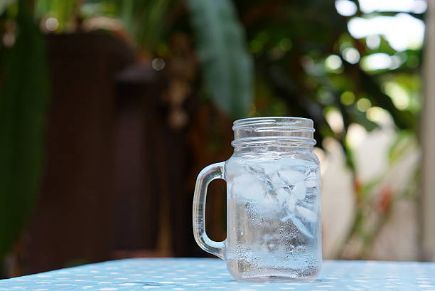freshness of ice water with ice cube in the glass jar on the blue table sheet with nature background