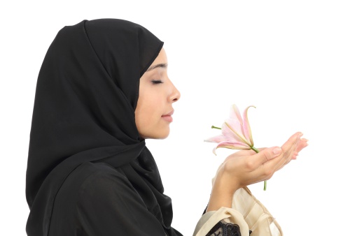 Close up of a profile of an arab woman smelling a flower isolated on a white background