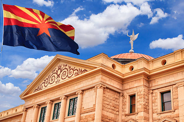 Arizona State Capitol Building State Capitol Building exterior in Phoenix, Arizona with wind blown US state flag outside on a partly cloudy day with Winged Victory weather vane on top of copper roof arizona stock pictures, royalty-free photos & images