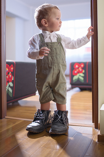 Young Caucasian boy standing in his father's shoes by the doorway