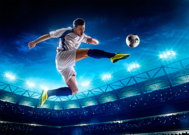 A soccer player kicking a ball in the air Soccer player in action on night stadium background kicking stock pictures, royalty-free photos & images