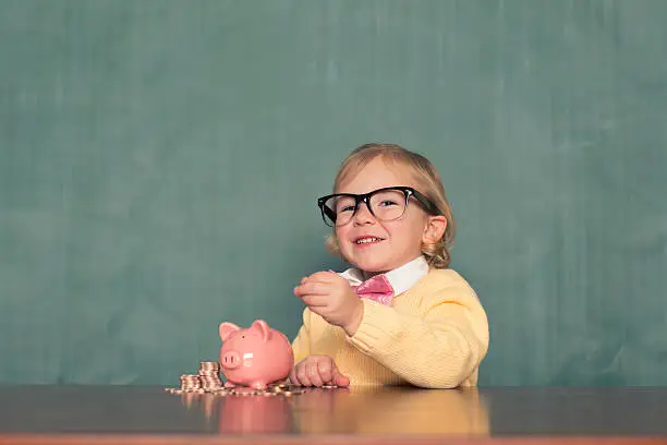 Photo of Young Girl Wearing Glasses Saves Money In Piggy Bank