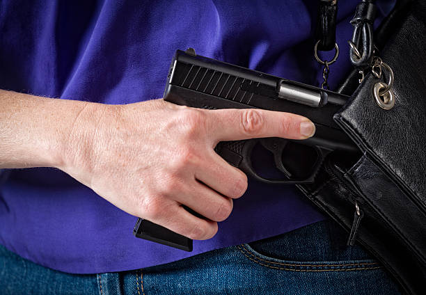 Woman Carrying Handgun A close-up of a woman holding a handgun in a purse. wallet gun stock pictures, royalty-free photos & images