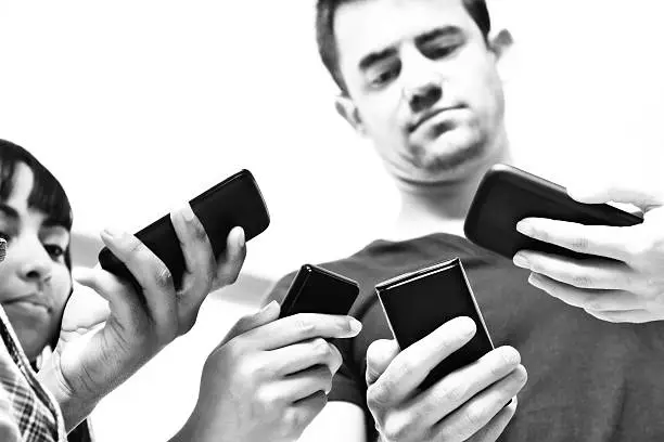 Four multi-ethnic male and female hands all busy checking their cell phones to see what's happening. Black and white, newspaper style image.