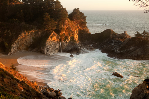 McWay Falls, a feature of the Julia Pfeiffer Burns State Park in the Big Sur area of the central California coast, drops 80 feet right onto the beach. Setting sun highlights the waves.