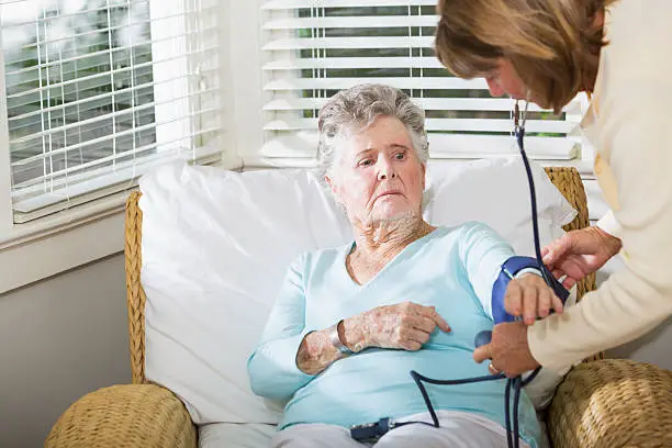 Caregiver (60s) checking blood pressure of elderly woman (90s).  Focus on elderly woman.