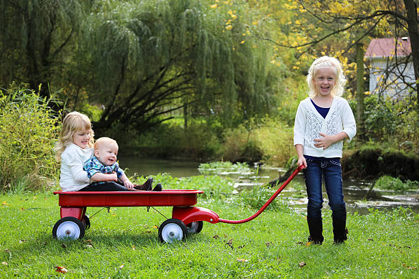 adorabile bambino tirando sorella e fratello ridere in red wagon - parker brothers foto e immagini stock