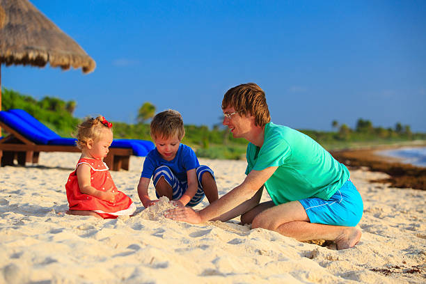 istock father and two kids playing with sand on the beach 466196558