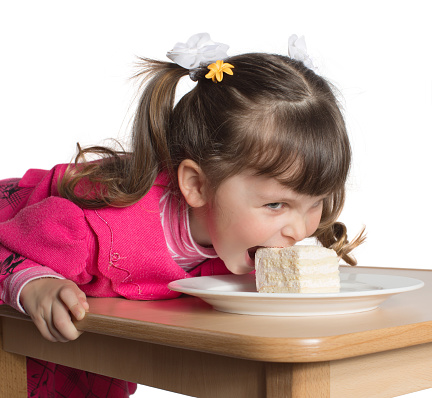 Charming preschooler in pink lays on table and eats cake. Little girl eating dessert