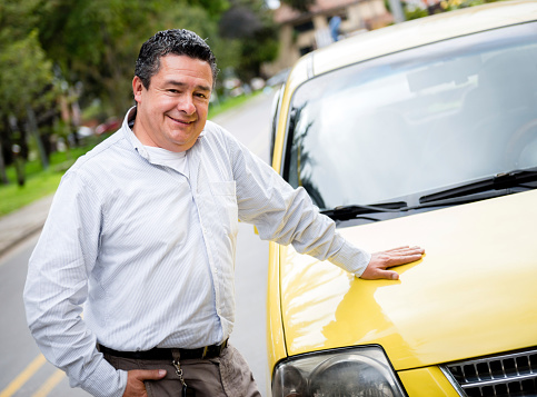 Proud taxi driver on the street with the car looking happy