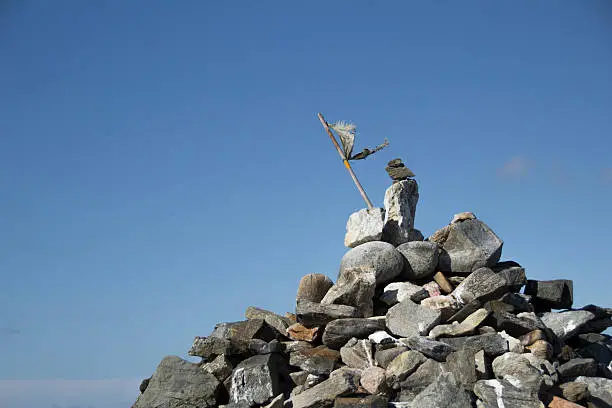Summit cairn with makeshift torn flag flapping in wind, against a blue sky