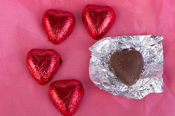 istock Four foil wrapped chocolate hearts with one unwrapped. 466199347
