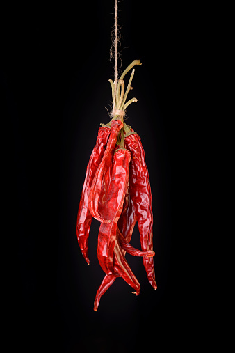 Hanged dry and sear hot red chili peppers isolated on black background