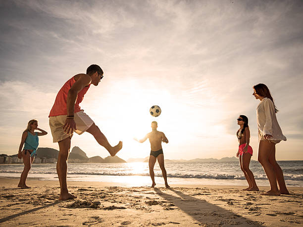 jovens jogando futebol na praia ao pôr do sol. - beach football imagens e fotografias de stock