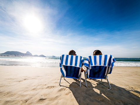 rear view of a Hispanic couple relaxing in deck chairs on the beach. Copy space.