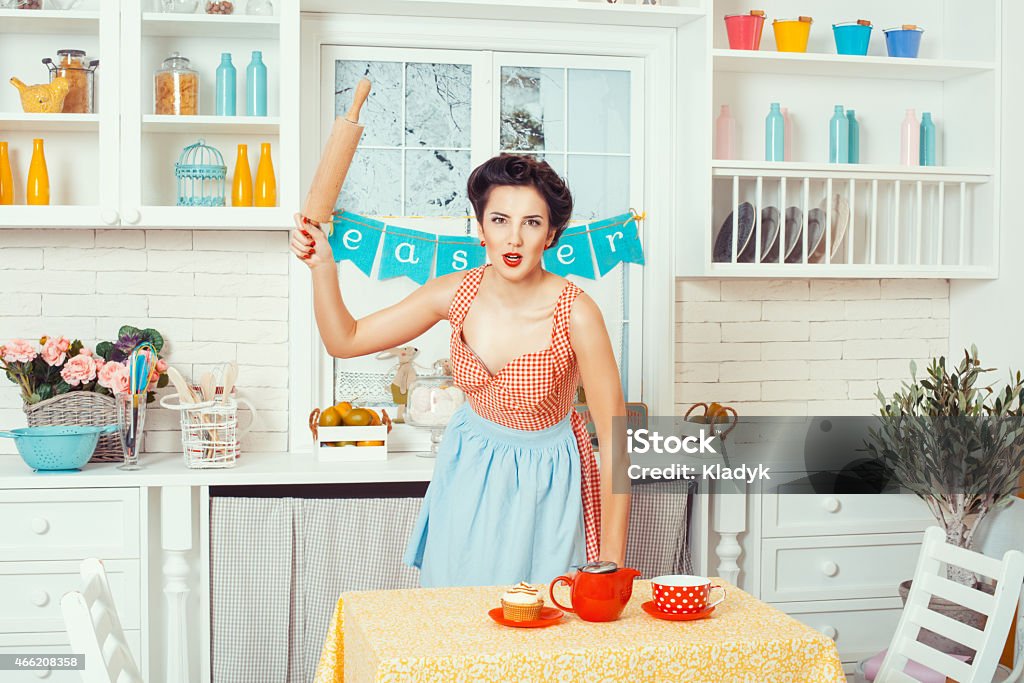 Girl waving rolling pin for the dough. Pin-up girl style. Girl standing in the kitchen and brandishing a rolling pin for the dough. 2015 Stock Photo