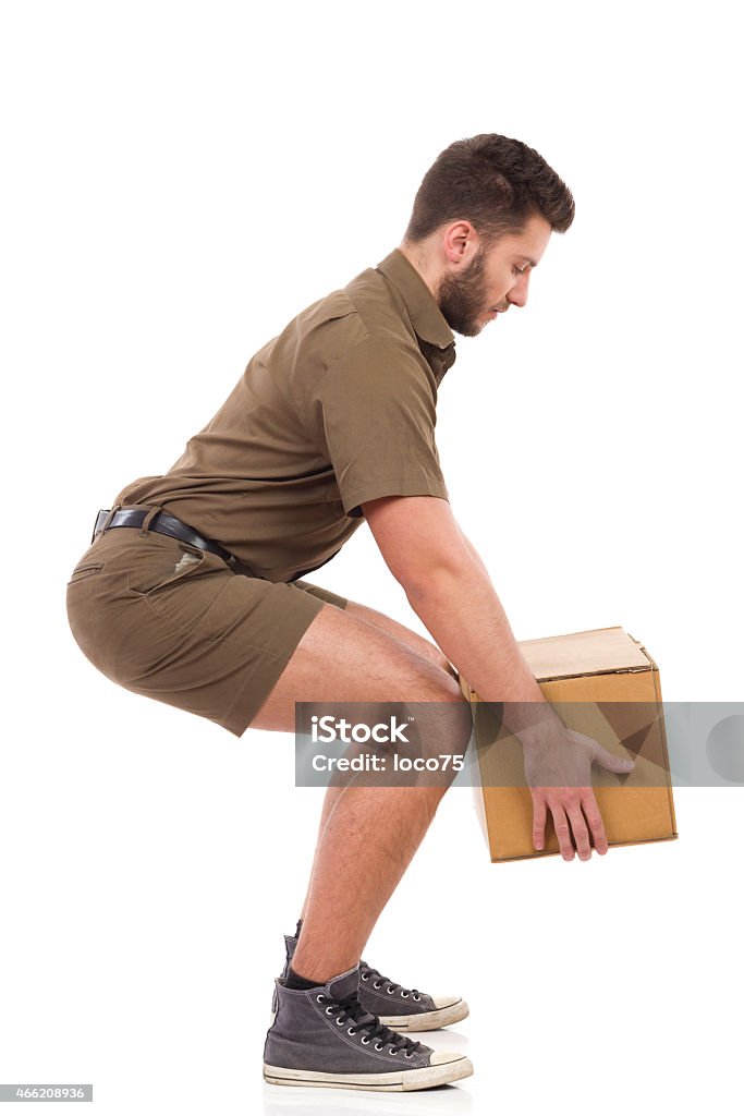 Courier picking up a package. Man in khaki uniform picking up a carton box, side view. Full length studio shot isolated on white. Picking Up Stock Photo