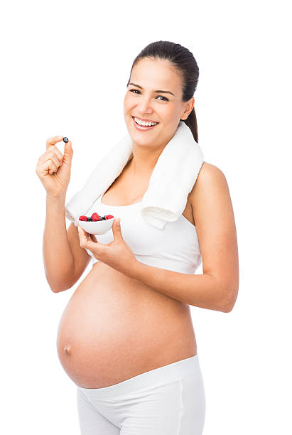 Happy pregnant woman eating berries A happy pregnant woman eating a small bowl of berries around her workout. Isolated on a white background. 8 months pregnant stock pictures, royalty-free photos & images