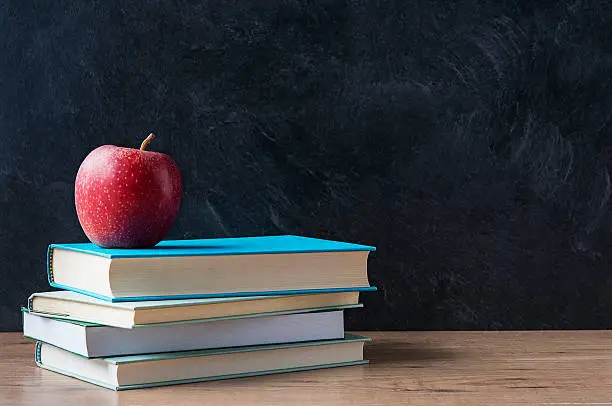 Photo of Apple on stacked books in front of a blackboard at school