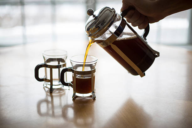 French Press Coffee Pour on a Cold Winter Morning. A back lit image of coffee being poured into small coffee mugs from a French Press with the light source being a window behind the table. glass cup of boiling water stock pictures, royalty-free photos & images