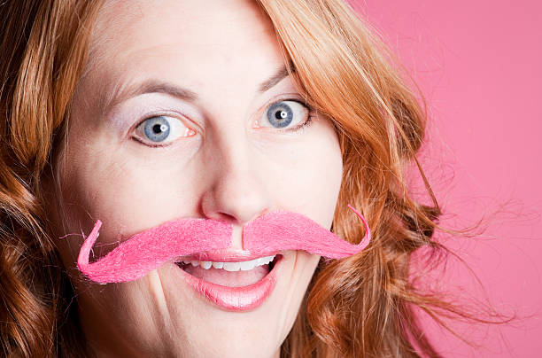 Smiling Woman Wearing Pink Handlebar Mustache A smiling woman wearing a pink handlebar mustache. women movember mustache facial hair stock pictures, royalty-free photos & images