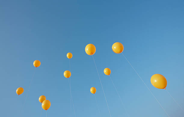 11 yellow balloons rising from the bottom seen in sunny blue sky
