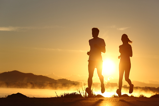 Silhouette of a couple running at sunset with the sun in the background