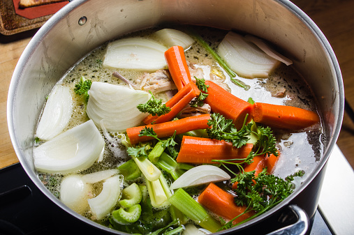 A large stock pot on a stove with vegetables cut for making soup