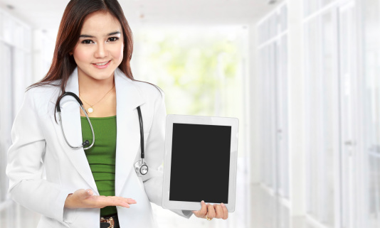 Copy-spaced portrait of female doctor wearing a white coat and stethoscope holding a tablet in hospital