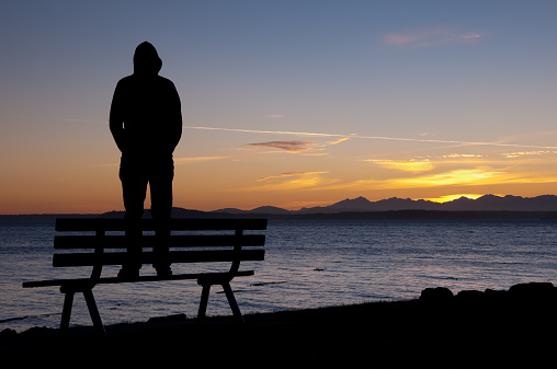 A silhouetted man standing on a bench at sunset over Elliott bay.