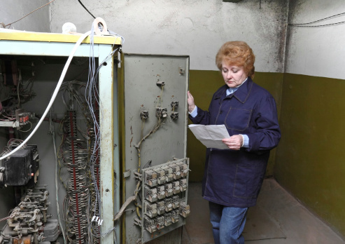 Operator woman-engineer in machine room (elevator) check the mechanical relay and cabinet.