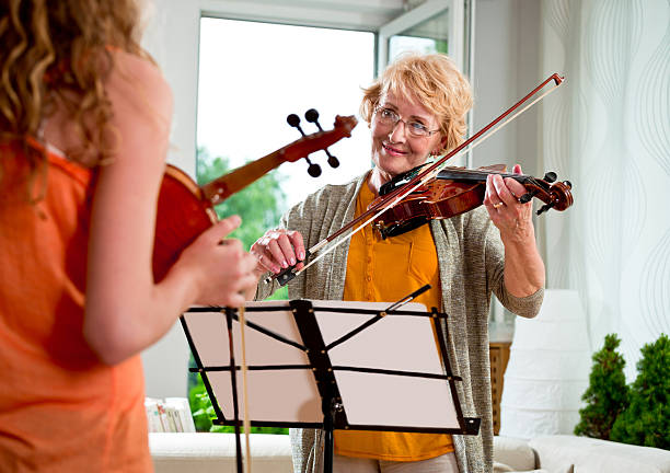 Smiling senior woman playing violin at home, looking at her sutdent.