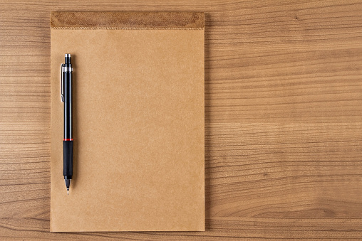 A blank craft reporters notebook with pencil on a wooden desk. The notebook on the left side of the photograph.