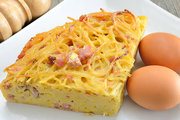 A slice of spaghetti frittata and two brown eggs on a plate spaghetti frittata with eggs cheese and bacon then fried in a pan frittata stock pictures, royalty-free photos & images