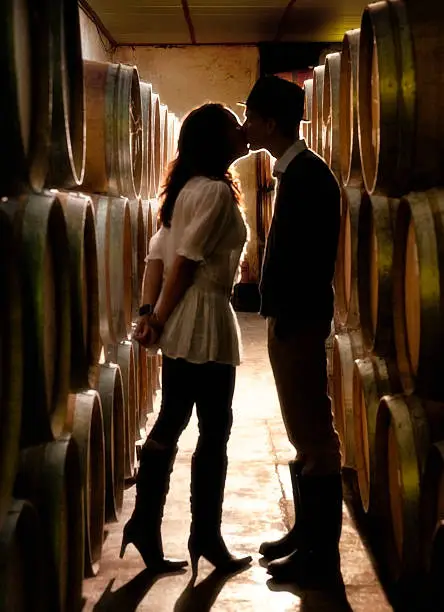 Photo of Soft view of couple kissing between oak barrels