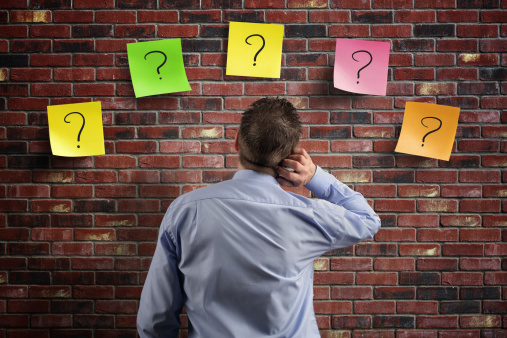 Choice and decisions businessman thinking with question marks written on adhesive notes stuck to a brick wall