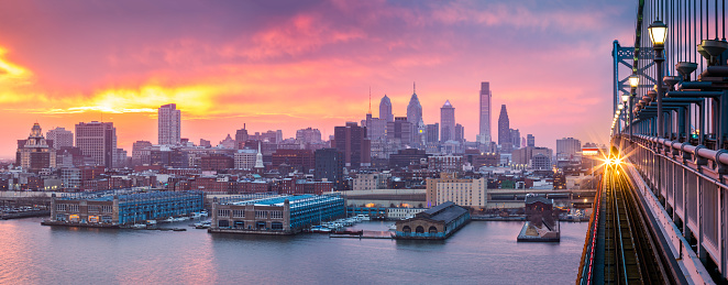 Philadelphia panorama under a hazy purple sunset. An incoming train crosses Ben Franklin Bridge.