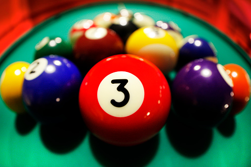 Cropped view on hand with orange billiard ball marked with number 13 on blurred background of gaming area