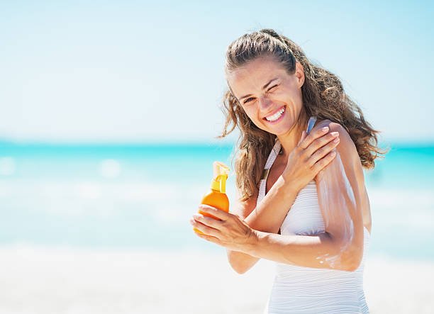 sorridente jovem mulher aplicar creme no bloco de sol praia - moisten imagens e fotografias de stock