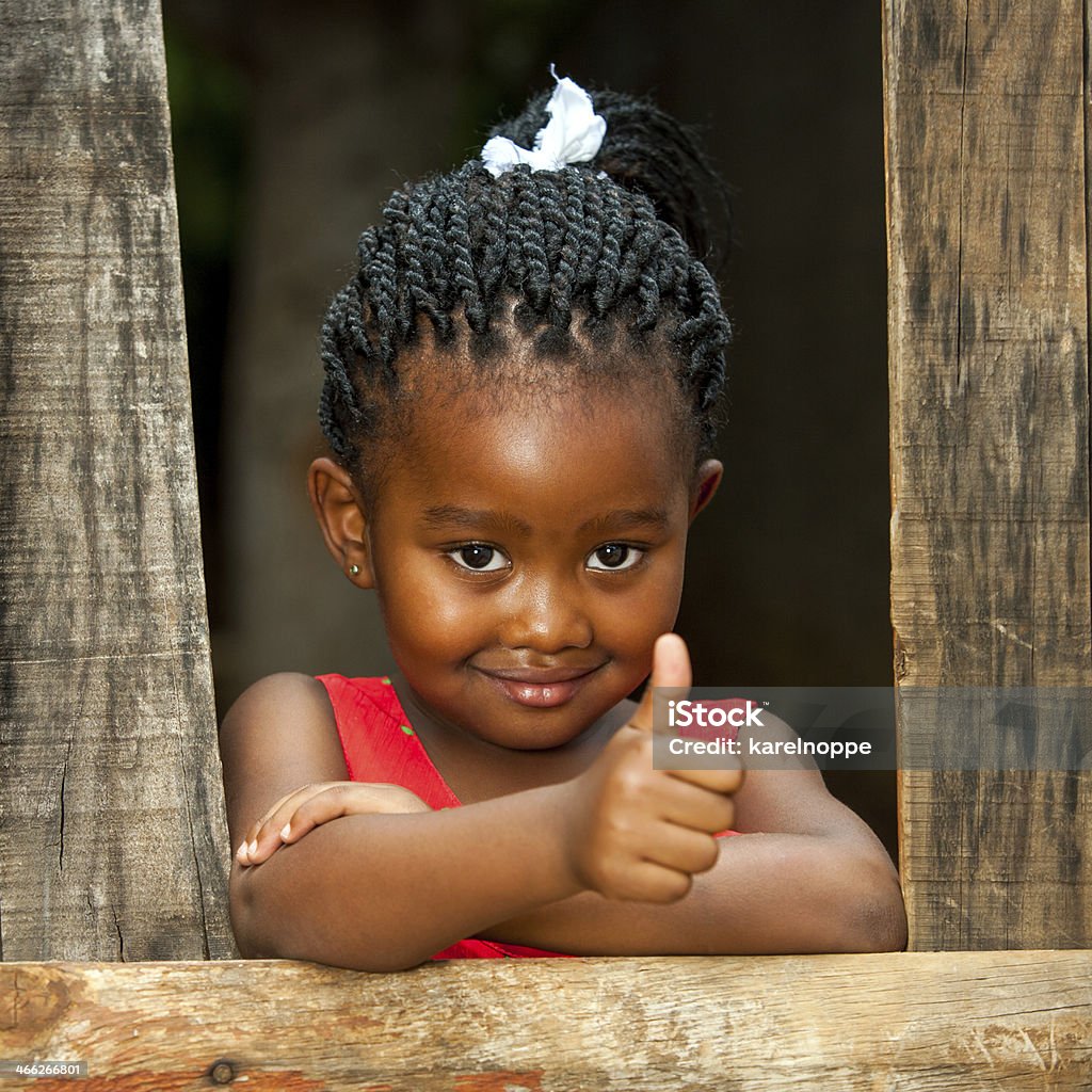 Little african girl at wooden fence with thumbs up. Portrait of small african girl doing thumbs up at wooden fence. African Ethnicity Stock Photo