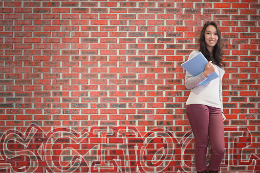 Smiling student holding notebook posing on brick background