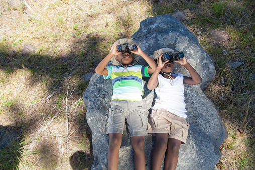 African boy and girl lying on a rock looking around throw their binoculars having fun. Cape Town, Western Cape, South Africa