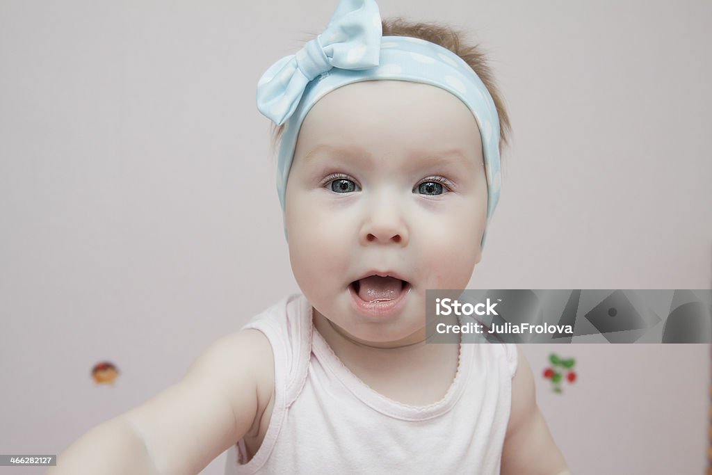 Beautiful baby with blue eyes opened her mouth The photo shows a little blue-eyed girl. She's sweet and funny, her head in her blue ribbon. The girl opened her mouth 12-23 Months Stock Photo