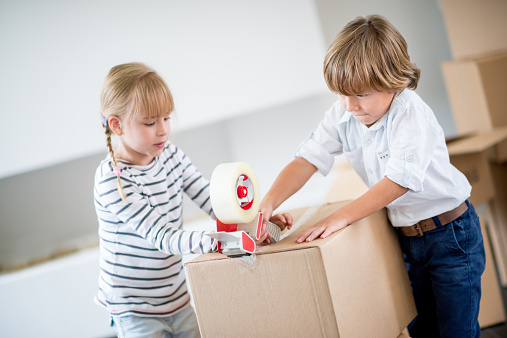 Kids packing and closing boxes with tape gun - moving house concepts